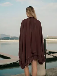 Achteraanzicht van bruine chiffon cape jurk met ruches zoom in buitenwateromgeving