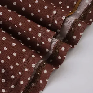 Detail of brown fabric with white polka dots showing overlock stitching at the hem.