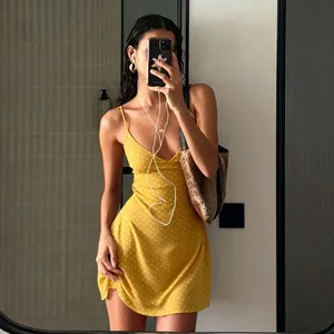 Full detail of a vibrant yellow polka dot mini slip dress worn in a casual mirror selfie