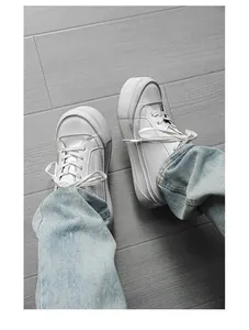 Men's low-top white platform sneakers paired with jeans on a wood floor view