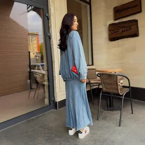 Woman wearing a stylish denim cardigan and long fishtail skirt in an outdoor cafe.