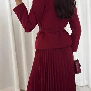 Elegante conjunto burdeos de dos piezas con blazer con cinturón y falda plisada.
