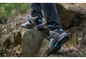 Side view of grey high-top men's hiking boots on rugged rocky forest trail.