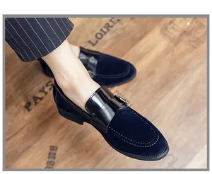 Close-up of navy blue velvet loafers with black leather strap details on a wooden floor