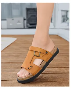 Nahaufnahme eines braunen Herren-Lederpantoffels an einem Fuß auf einem Holzfußboden.