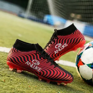Primer plano de botas de fútbol de caña alta rojas y negras con ondas en campo verde