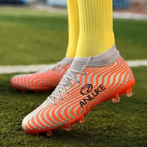 Detalle de botas de fútbol AG altas con patrón ondulado naranja y tacos en campo.