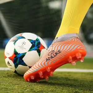 Vista macro de botas de fútbol altas naranjas y plateadas con tacos AG en césped artificial.