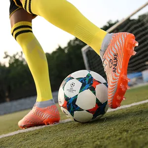 Primer plano de botas de fútbol naranjas de caña alta con tacos AG en campo de césped.