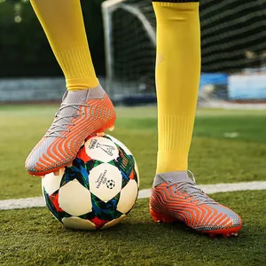 Detalle de botas de fútbol de caña alta naranjas con tacos AG en campo de césped