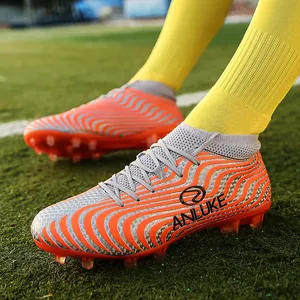 Primer plano de botas de fútbol de rayas naranjas y plateadas con logo ANLUKE en césped verde.