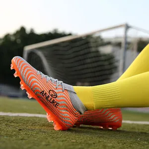 Vista lateral de botas de fútbol de caña alta naranjas y grises en césped.