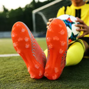 Primer plano de la suela de botas de fútbol AG naranjas con tacos deportivos