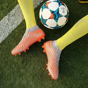 Primer plano de botas de fútbol naranjas y plateadas en césped con balón de fútbol