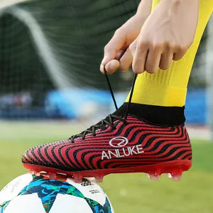 Primer plano de botas de fútbol AG rojas y negras atándose en un campo de fútbol