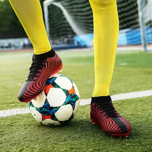 Botas de fútbol de caña alta profesionales con rayas rojas y negras para entrenamiento de césped.