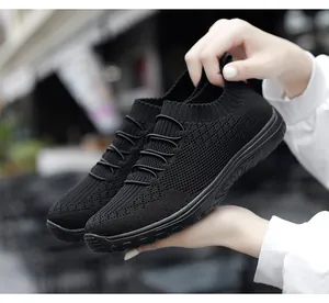 Detail view of black breathable flyknit mesh women's slip-on sneakers held by hands