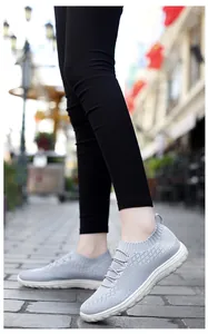 Side view of light grey fly-knit mesh women's sneakers worn by model on city street