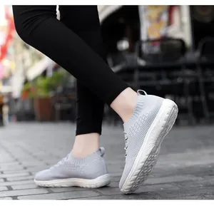 Side view of grey mesh slip-on sneakers on a model walking on a stone street