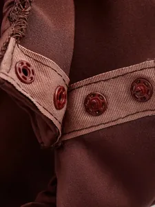 Macro detail of the brown satin bodysuit showing secure snap button closure and fabric texture