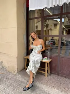 Lifestyle shot of a woman in a white polka dot midi dress at an outdoor cafe.