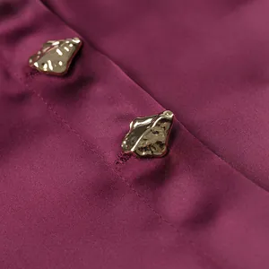 Detailed macro shot showing irregular golden buttons on elegant burgundy satin shirt