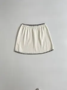 Close-up detail of a white knitted mini skirt with black contrast stitch embroidery.