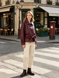 Detail view of a burgundy faux leather short trench coat with belt in a street setting
