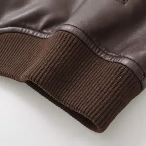 Close-up macro detail of vintage brown faux leather bomber jacket showing ribbed knit cuff texture