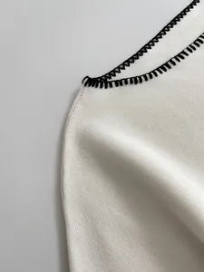 Close-up of white knit fabric with decorative black blanket stitch embroidery detail