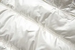 Close-up of white metallic shiny fabric on padded jacket with quilting detail