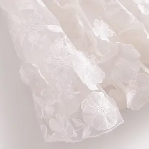 Exquisite close-up of white 3D floral lace embroidery on delicate sheer mesh fabric