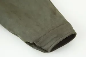 Detailopname van de manchet van een olijfgroen jasje met stiksel en suède-achtige textuur.