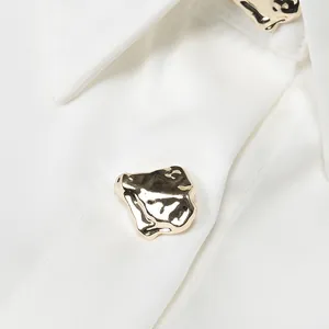 Close-up detail of a textured golden irregular button on a white satin blouse collar