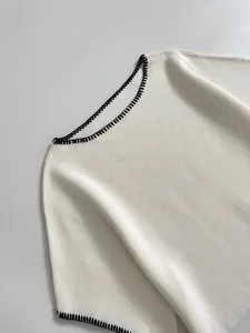 Close-up of elegant white knitted top with decorative black contrast whipstitch embroidery