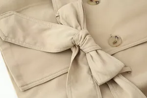 Detailopname van een kaki trenchcoat met dubbele rij knopen en tailleband met strik