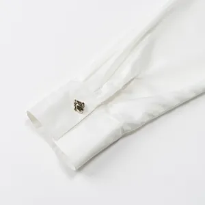 Detailed macro view of an elegant white satin shirt sleeve with unique gold button.