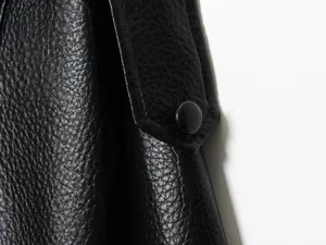 Detailaufnahme einer schwarzen Kunstlederjacke mit Narbenleder-Textur und Knopfübersicht