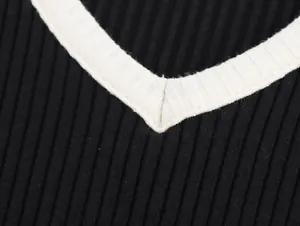 Macro view of the white layered V-neckline detail on a black ribbed knit sweater fabric.