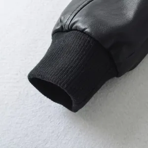 Detail of black faux leather bomber jacket showing ribbed knit cuff and texture.
