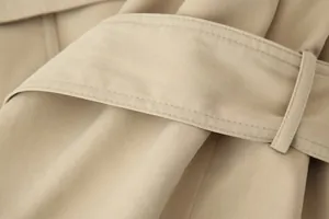 Macroweergave van de hoogwaardige stiksels en de riemlus van deze kaki trenchcoat