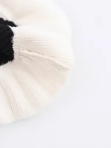 Close-up macro view of a layered v-neck knit sweater with cream and black ribbed texture.