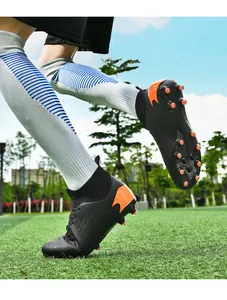 Foto de acción de botas de fútbol altas negras y naranjas en campo de césped artificial