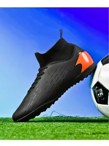 Zapatillas de fútbol de caña alta profesionales en negro y naranja sobre césped artificial