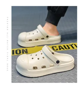 Nahaufnahme cremeweißer Clogs mit dicker Sohle und atmungsaktivem Lochdesign auf Metallboden.