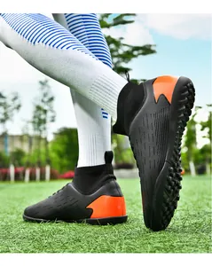 Botas de fútbol turf negras y naranjas de caña alta en acción sobre césped