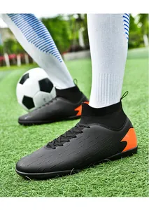 Perfil lateral de botas de fútbol negras de caña alta con detalles naranja en césped