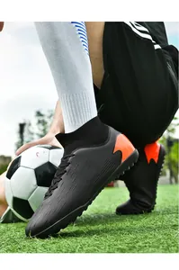 Primer plano de botas de fútbol de caña alta negras y naranjas para hombre en el césped