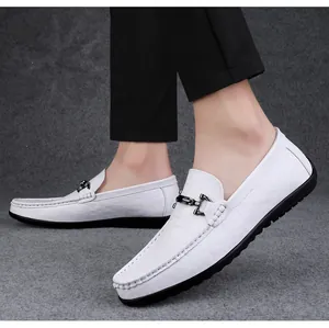 Detail view of white men's leather loafers with metallic buckle on grey background.
