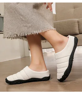 Close-up of white quilted winter slippers with black non-slip textured rubber soles